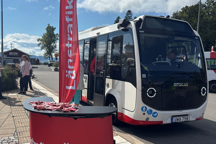 Bilden visar den nya elbussen i Hamnen på Visingsö. Bussen är ganska liten. Några personer står intill bussen och pratar.