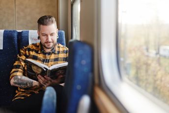 Bild på manlig resenär som läser bok ombord på tåget