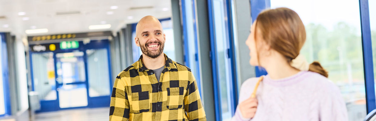 En bild som visar två resenärer, en kvinna och en man. De ser på varandra och ler. 