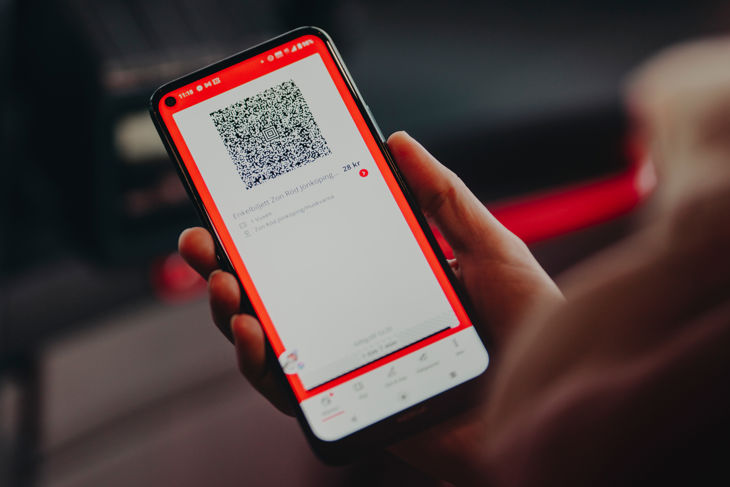Bild på en hand som håller i en mobiltelefon. Mobiltelefonen visar JLT:s app och en giltig biljett med QR-kod som ska blippas i läsaren på bussen. 
