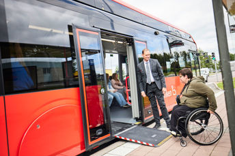 Resenär i rullstol får hjälp med ramp av föraren för att kunna rulla ombord på bussen.  