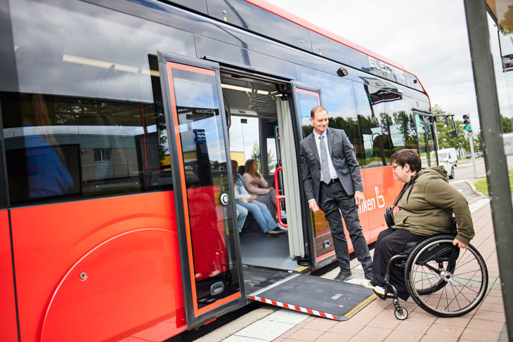 Resenär i rullstol får hjälp med ramp av föraren för att kunna rulla ombord på bussen.