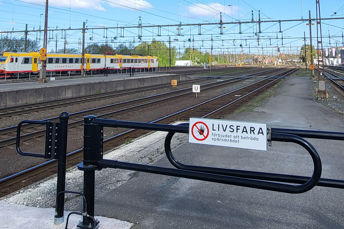 Bild på järnvägsområde med avspärrning. Skylt på avspärrning med texten "Livsfarligt". 