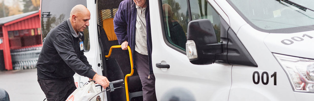 Bilden visar en förare som hjälper en resenär att kliva ut ur en serviceresebuss. 