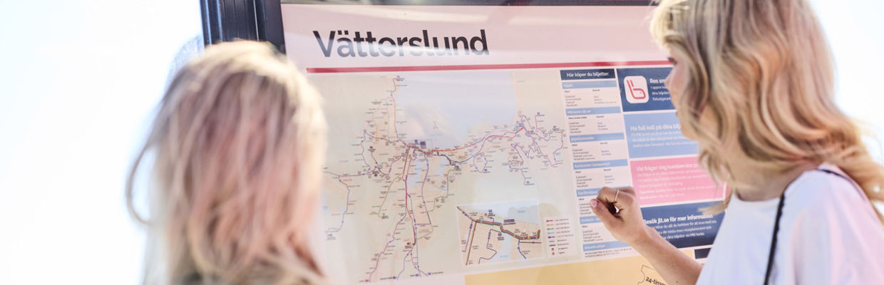 Två resenärer står vid en hållplats och läser på en karta.