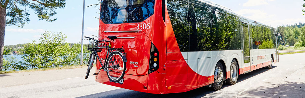 En regionbuss som kör på en landsväg. Bussen har en cykel på hållaren bak på bussen. 