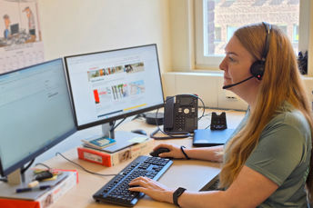 En medarbetare på JLT sitter och jobbar framför en dator och svarar i telefon genom headset.
