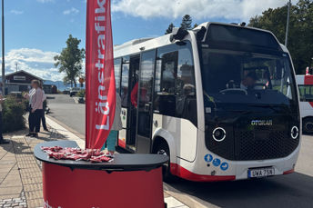 Bilden visar den nya elbussen i Hamnen på Visingsö. Bussen är ganska liten. Några personer står intill bussen och pratar.